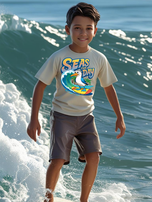 Child wearing a crew neck 'Seas the Day' t-shirt with surfing booby graphic standing on a surfboard in ocean waves